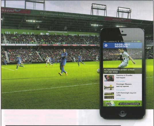 smartphone displaying the DVHN app, with the Euroborg pitch and players visible in the background from FC Groningen matchday programmre 2015
